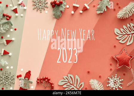 Text Happy New Year 2023. Winter decor: silver leaves, doll and snowflakes. Top view on layered paper background in red, pink and silver grey. Stock Photo