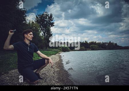 Sad guy on the beach throwing away his black mask Stock Photo