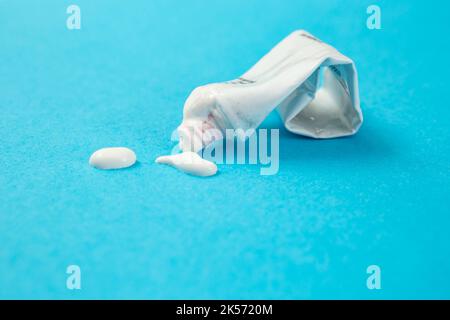 White paint almost empty tube wit paint splatter isolated on blue background. Stock Photo