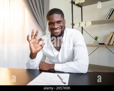 Business agreement. Successful project. Well done. Satisfied cheerful man approving contract with okay gesture at office workplace interior. Stock Photo