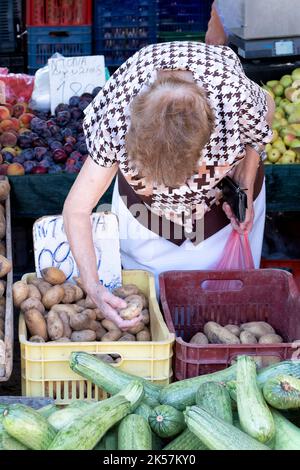 An elderly woman is shown sorting through and choosing potatoes on a vegetable stall in the Laiki, the peoples street market in Rhodes City, Rhodes Stock Photo