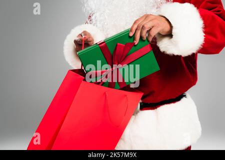 Cropped view of bearded santa claus putting present in shopping bag isolated on grey,stock image Stock Photo