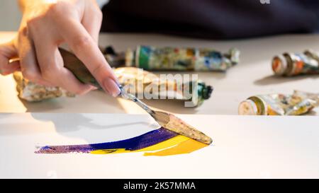 Painting lesson. Creative process. Artistic tools. Hobby leisure. Unrecognizable woman mixing blue yellow paint colors with palette knife on canvas. Stock Photo