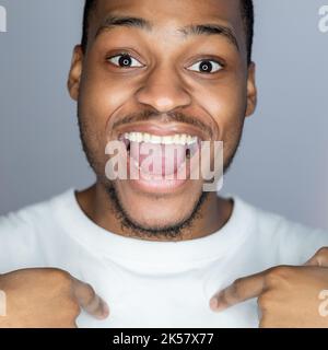 Male confidence. Self acceptance. Motivation approval. Portrait of happy astonished handsome African man in white showing love myself smiling isolated Stock Photo