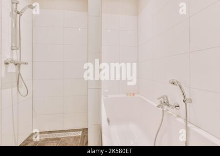 Bathtub located near shower box with glass door in modern bathroom with white tiled walls Stock Photo