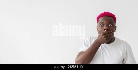 Shocked news. Surprised black man. Unexpected situation. Gossip rumors. Bewildered african guy with bright pink hair closing mouth hand isolated white Stock Photo