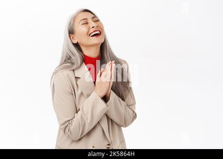 Portrait of beautiful middle-aged asian woman with grey hair, clap hands, smiling and laughing happy, standing over white background Stock Photo