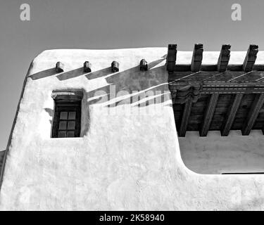 A black and whie image of an adobe building with a window and wooden beams in Santa Fe, New Mexico Stock Photo