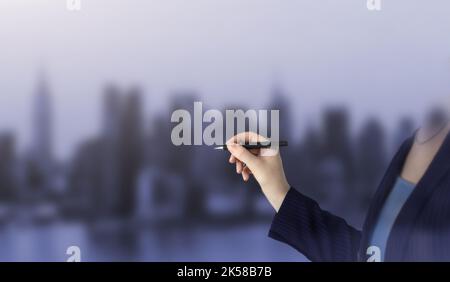 Female hand writing with a pen on city background, black pen in hand. Closeup of hand holding a black marker about to write something Stock Photo