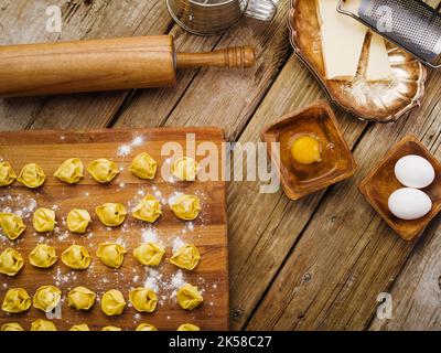 On a wooden kitchen table, homemade dumplings stuffed with minced meat on a cutting board, kitchen utensils and ingredients. Low angle view. Recipes f Stock Photo