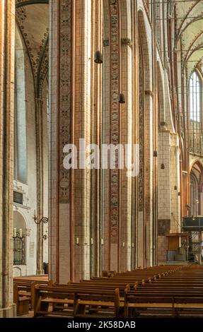 Germany, Lubeck - July 13, 2022: Marienkirche. Colored decorated pillars and arches reaching from floor with wooden benches up to ceiling Stock Photo