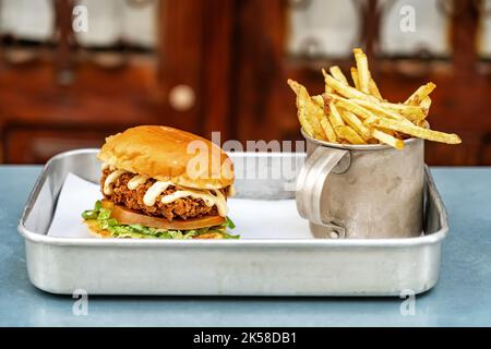 Classic hamburger with meat salad mayonnaise and fried potatoes in an aluminum mug on a tray. Close-up. Stock Photo