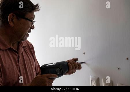 latino man using a power drill to drill holes in the wall to hang a new television, drilling holes in the wall, mexican, hispanic Stock Photo