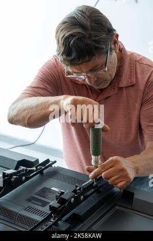 Mexican Latino man repairing a TV screen, checking for faults. Stock Photo