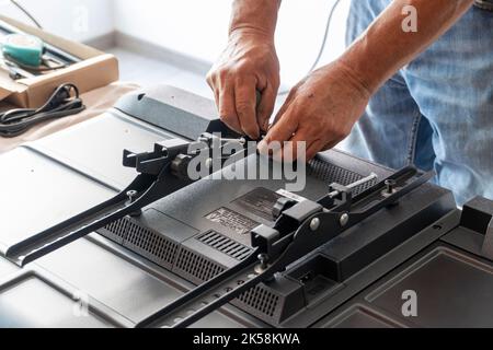 man installing the wall base for the television, it is a smart tv, adjusting with screwdriver Stock Photo