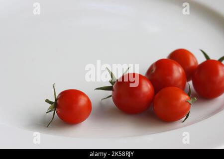 Bunch of fresh, red tomatoes with green stems isolated on white plate. White background. Clipping path. Stock Photo