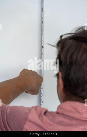Senior man measure wall with measuring tape repairing apartment. Mature husband redecorate house Stock Photo