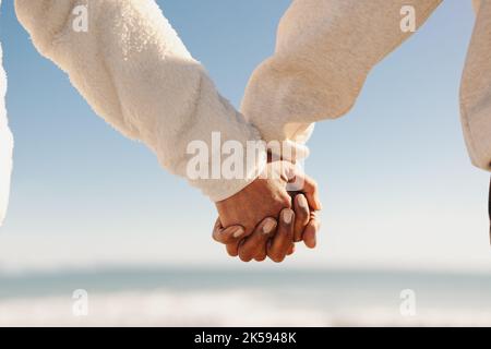 Mature couple holding hands while standing on a wooden foot bridge at the beach. Romantic senior couple taking a refreshing seaside holiday after reti Stock Photo