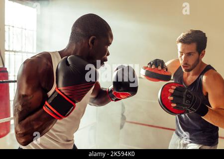 Athletic young man working on punching combinations with the focus mitts held by his personal trainer. Young boxer having a training session with his Stock Photo