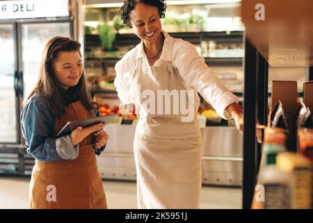 Friendly shop owner having a discussion with her new employee in a grocery store. Female small business owner giving a woman with Down syndrome traini Stock Photo