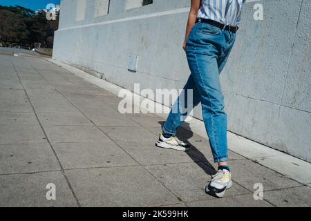 Close-up of a woman's legs walking down the street wearing jeans and sneakers. Concept of feminine, healthy life, fashion. Copyspace. Stock Photo
