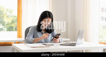 Business woman or accountant hand using mobile smart phone and laptop computer with documentary data graph paper on the table at modern home office Stock Photo