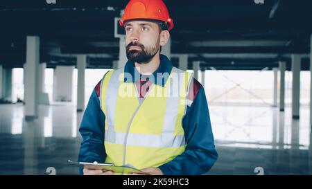 Construction inspector wearing uniform is checking papers and studying industrial building inside. Supervision and hse inspection concept. Stock Photo
