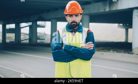 portrait of field engineer standing in industrial area with arms crossed and looking at camera. Construction and specialists concept. Stock Photo