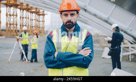 Portrait of construction employee wearing uniform standing outdoors in workplace with arms crossed and looking at camera. Career and people concept. Stock Photo