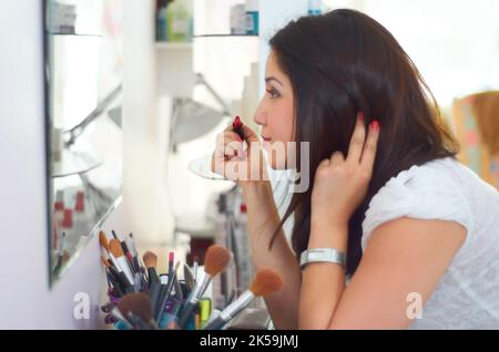 Light up your face. an attractive young woman applying makeup in the bathroom. Stock Photo