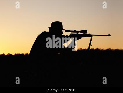 Hunting the hunter. A silhouette of a man in the outdoors holding up his sniper rifle. Stock Photo
