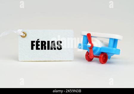On a white surface there is a toy airplane and a sign with the inscription - VACATION TIME. Text in Portuguese. Stock Photo