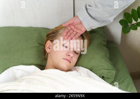 Mom touches her hand to the forehead of a sick daughter lying on the bed. Checks temperature. The concept of health and medicine. Stock Photo