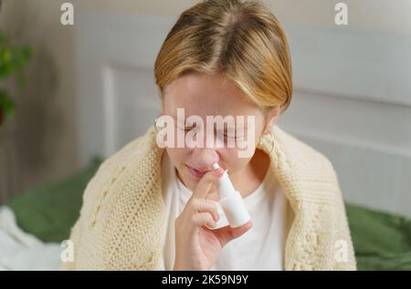 A girl with a cold treats a runny nose with a nasal spray. Medicine and health concept. Stock Photo