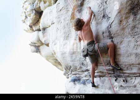 Hes excellent at what he does. A rock climber climbing a steep cliff face. Stock Photo