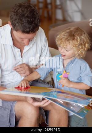 Talented toddler at play. A smiling toddler boy holding and fitting puzzle pieces while his father holds a puzzle book. Stock Photo