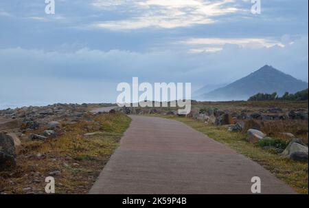 Aerial view of road and mountain on Atlantic ocean coast. Stones and rocks with moss on road along ocean. Camino de Santiago way in morning haze Stock Photo