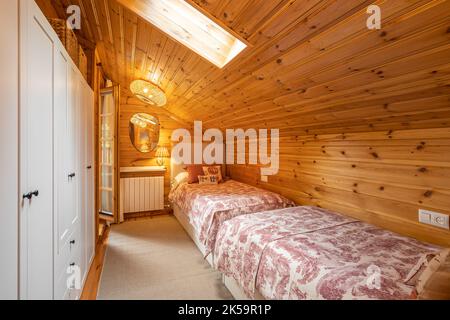 Cozy bedroom with two beds and white wardrobe in a modern cottage with wooden walls. Stock Photo
