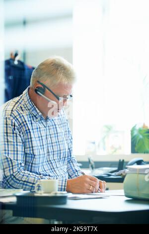 He strives for perfection in everything he does. A senior businessman wearing a headset writing down notes while on the phone at his desk. Stock Photo