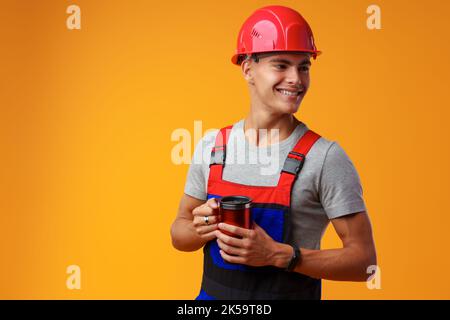 Young builder in uniform holding coffee cup on yellow background Stock Photo
