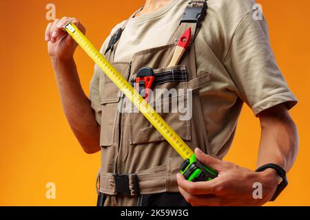 Close up of builder holding measuring roulette against yellow background in studio Stock Photo