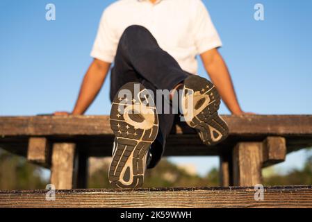 A man wearing running shoes with worn-out outsole is sitting on a bench table Stock Photo