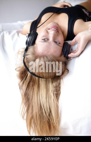 This is my favorite song. a beautiful young woman listening to music while relaxing on her bed. Stock Photo