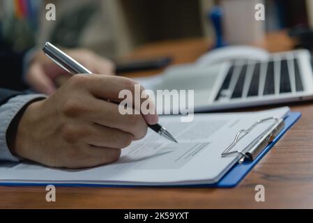 Hand holding pen writing paperwork business document financial investment or signature contract job and insurance on desk. Stock Photo