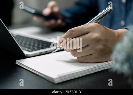 Man hand with pen writing on notebook with computer laptop at desk. Stock Photo