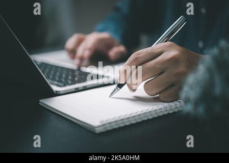 Man hand with pen writing on notebook with computer laptop at desk. Stock Photo
