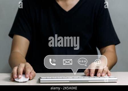 Hotline for customer support Contact us for people connection. Businessman using computer keyboard with email, phone, address, and chat message icons. Stock Photo