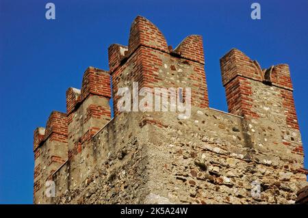 Swallowtail battlements built in brick crown the main towers of a medieval castle, the Castello Scaligero or Rocca Scaligera, at Sirmione, Lombardy, Italy.  Built in the 1300s, the castle takes its name from the Della Scala family, ruling dynasty in Verona, who dominated the area at the time.  It is one of the best-preserved Scaliger fortresses. Stock Photo