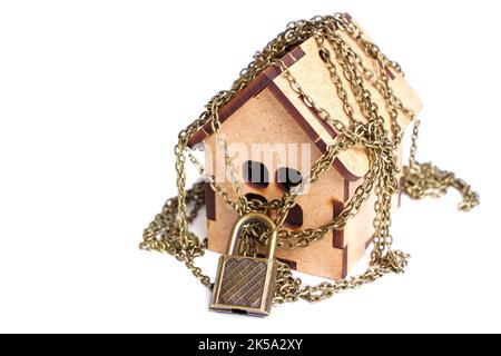 Wooden house wrapped with chains secured with a padlock on white. Stock Photo