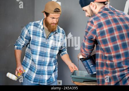 Construction workers men holding paint roller tool in house room renovation. Painter preparing paint and construction tools near concrete or plaster Stock Photo
